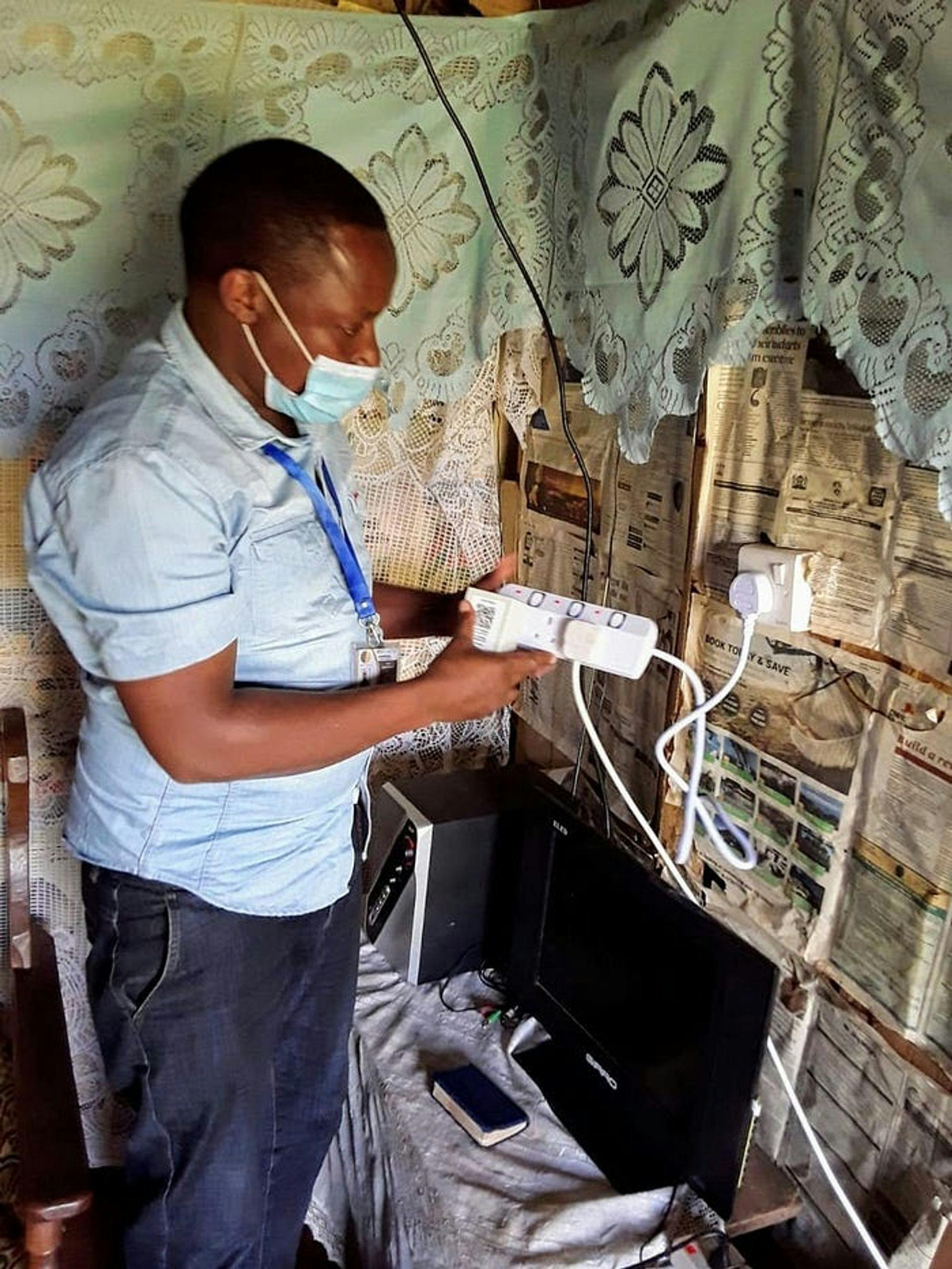 A Field Officer installing the PowerWatch device at a participant’s home in Western Kenya. Power strips are provided to ensure the device does not take the space of an available outlet. (Photo credit: Solomon Mutai)